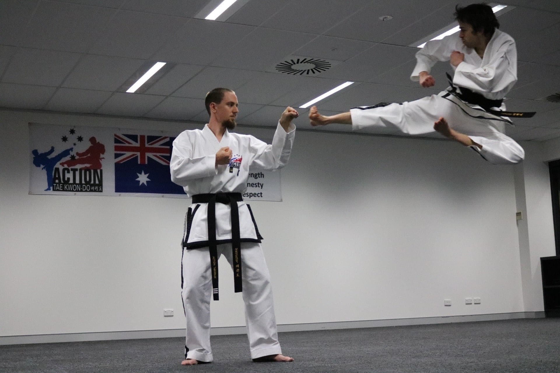 Black belt adult and instructor students of action tae kwon do performing a flying side kick.