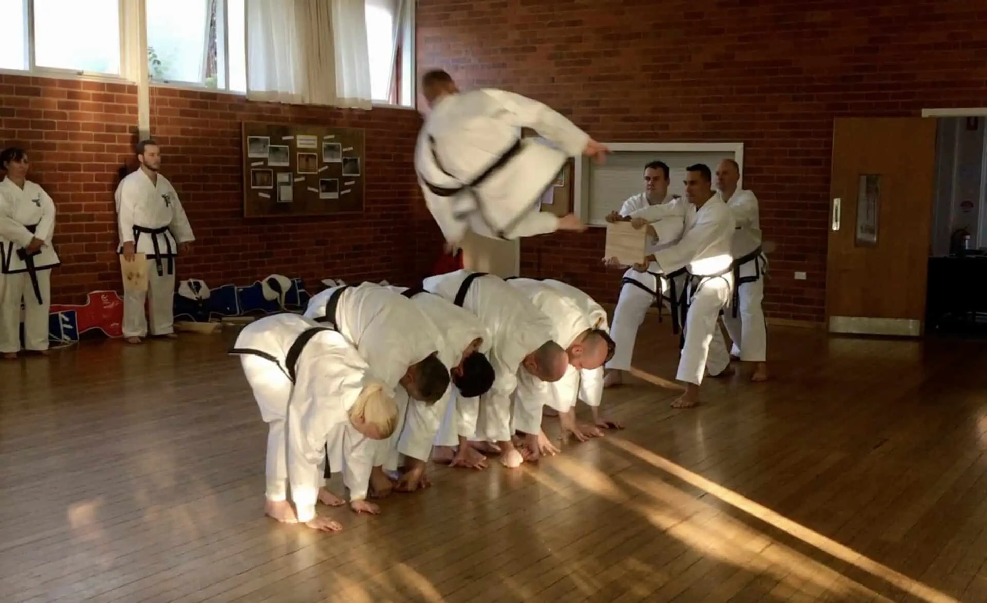 Chief Instructor Alex flying over 5 black belts while performing a flying side kick.